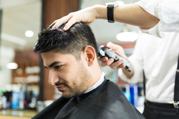 Fototapeta premium Male Receiving Haircut By Barber Using Trimmer In Salon