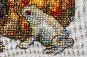 Cross-stitch embroidery with cat in hat, cauldron, toad, bonfire and pumpkin.