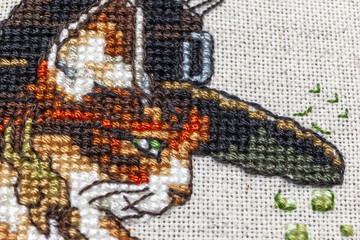 Cross-stitch embroidery with cat in hat, cauldron, toad, bonfire and pumpkin.