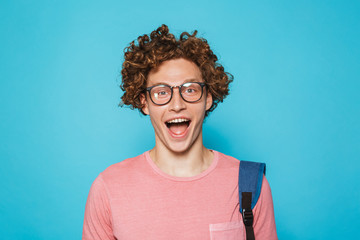 Image of geek guy with curly hair wearing glasses and backpack smiling at camera, isolated over...