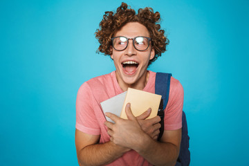 Photo of nerd student guy with curly hair wearing glasses and backpack laughing and holding books,...
