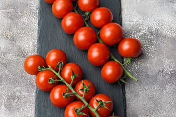 Fototapeta na wymiar Fresh cherry tomatoes on a branch on a black concrete background. Top view