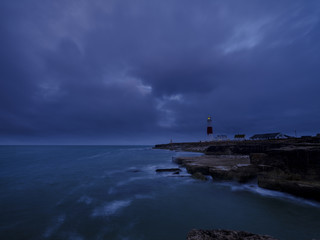 Fototapeta premium Summer sunrise with stormy clouds and slow shutter speed at Portland Bill Light, Dorset, UK