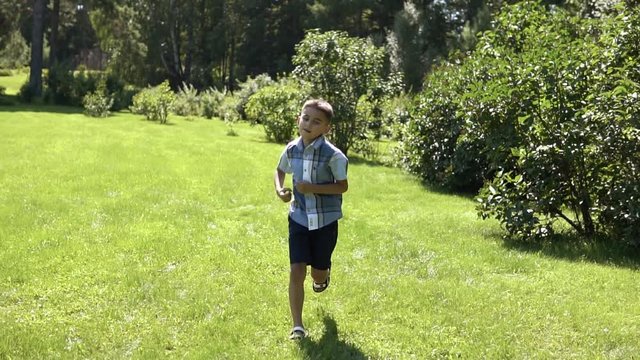 An attractive boy runs along the grass in the park having a good mood in sunny weather. slow motion. HD