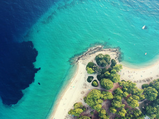 Aerial view of bright turqoise water and beach with pine forest.