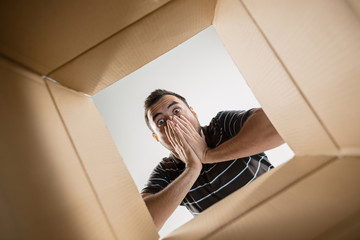 The surprised man unpacking, opening carton box and looking inside. The package, delivery,...