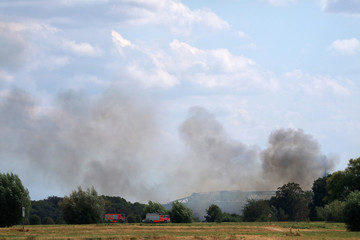Fototapeta na wymiar Brennendes Buschgelände mit Feuerwehrfahrzeugen im Vordergrund