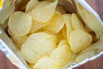 Potato chips in open snack bag close up on table floor