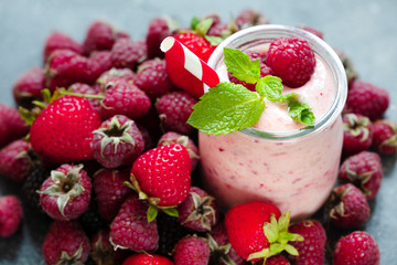 Pink berry smoothie or milk shake in glass jar with fresh raspberry and strawberry background, top...