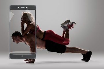 fitness, sport, training, teamwork and lifestyle concept - man starts out push-ups and girl lying on him and rests. full length grey background. conceptual collage with device
