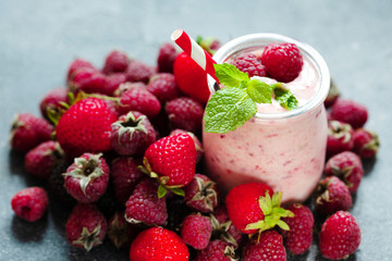 Pink berry smoothie or milk shake in glass jar with fresh raspberry and strawberry background, top view