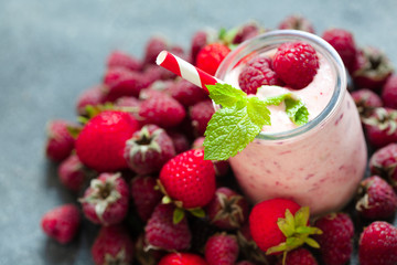 Pink berry smoothie or milk shake in glass jar with fresh raspberry and strawberry background, top view