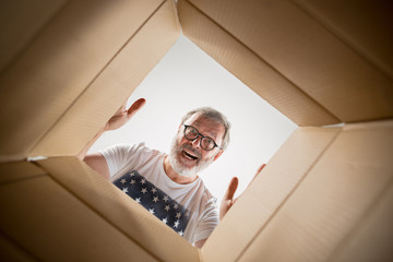 The surprised senior man unpacking, opening carton box and looking inside. The package, delivery,...