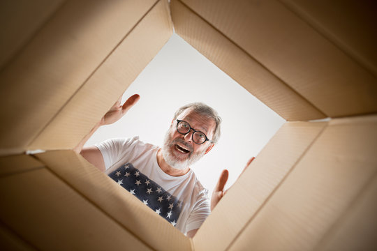 The surprised senior man unpacking, opening carton box and looking inside. The package, delivery, surprise, gift lifestyle concept. Human emotions and facial expressions concepts