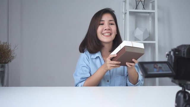 Happy beautiful Asian woman unboxing gifts from brand or her subscribers. Female blogger recording video from camera to fliming an unboxing video.