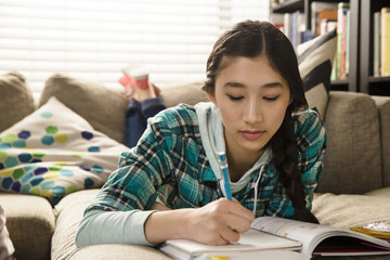 Girl doing homework while lying on couch at home