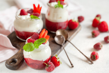 Jars of natural white yogurt with berry sauce decorated with fresh strawbeery, raspberry and mint