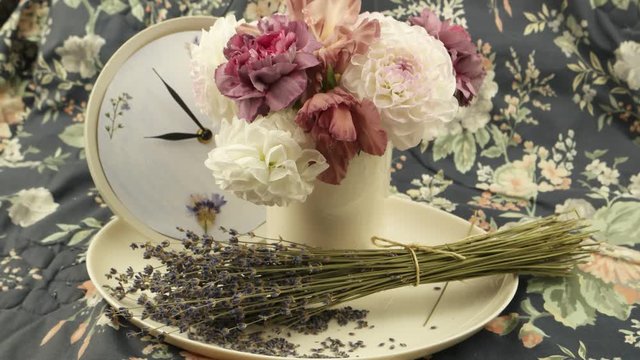 White dahlias in the vase, a clock and a bouquet of dry lavender on the fabric with flower pattern, floral composition