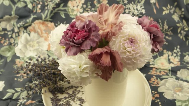 White dahlias, pale pink carnations in a vase  and a bouquet of dry lavender against of  fabric with a floral pattern, a floral arrangement