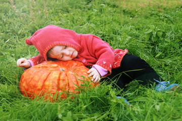 a little girl lie down on a huge pumpkin in a magical meadow. The baby is wearing a gnome costume. Magic and fireflies. Can be used as a card for halloween holiday