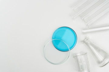top view of laboratory equipments. A blue liquid watch glass, flask, test tubes and beaker on the...