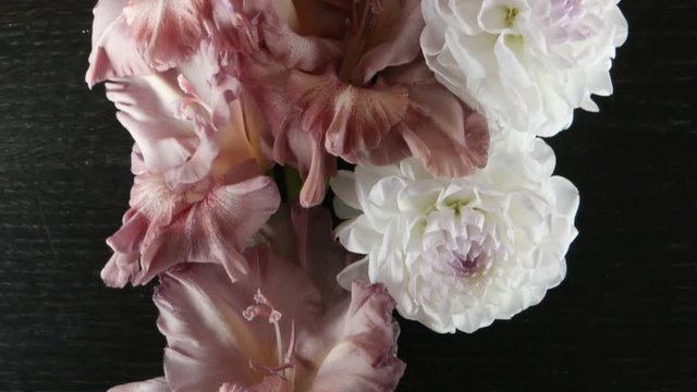 The gladiolus of pale pink color and white dahlias are lying on a black wooden table, floral arrangement