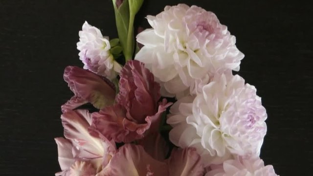 The gladiolus of pale pink color and white dahlias are lying on a black wooden table, floral arrangement