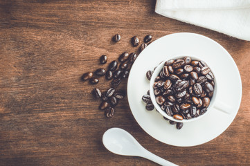 Roasted coffee beans with white ceramic cup and spoon on wooden table.