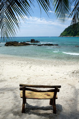 hand made wooden seat on a deserted white sandy tropical beach and blue sea.