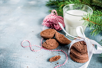 Festive Christmas greeting card background with natural Fir Spruce branches, chocolate cookies, milk glass. Christmas treat for Santa Claus, light blue background copy space