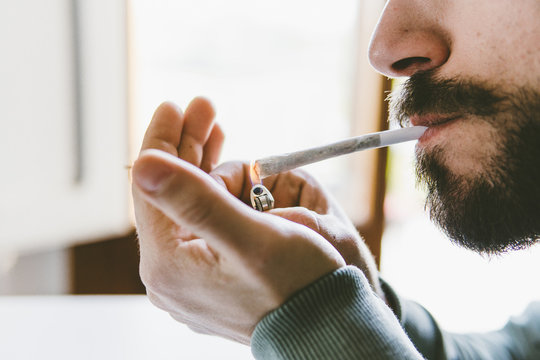 Midsection of bearded man igniting marijuana joint with cigarette lighter at home