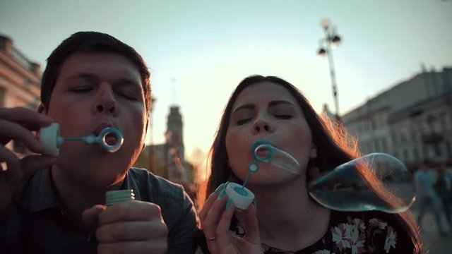 Love and soap bubbles blowing by male and female young married couple. Slow motion shot on the street. Cool evening teal and orange colored footage. Fun and happiness.