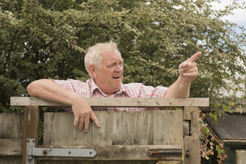 Mature man shouting and pointing over a fence in the garden 