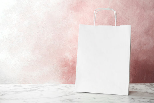 Mockup of paper shopping bag on table against color background