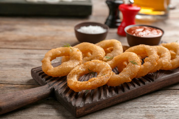 Wooden board with fried onion rings on table