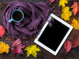 Still life of cup of coffee, scarf,autumn leaves and tablet on brown wooden background