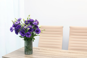Beautiful bouquet in vase on wooden table against color background. Stylish interior