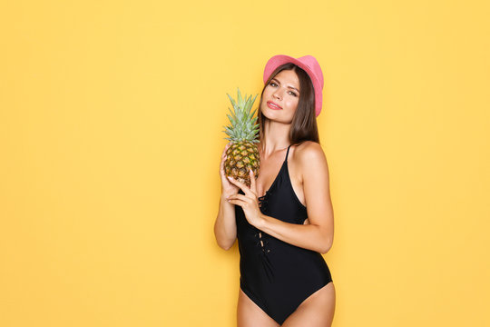 Sexy young woman in bikini with pineapple on color background