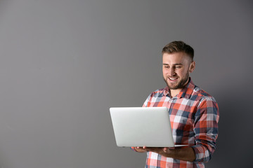 Young man with laptop on grey background