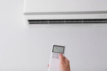 Fototapeta premium Woman operating air conditioner with remote control indoors, focus on hand