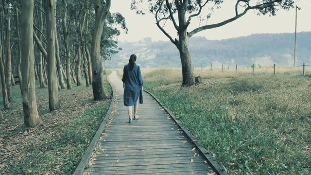 4k pretty young girl walking on the natural wooden podium in the beautiful nature grove with green hills on the background