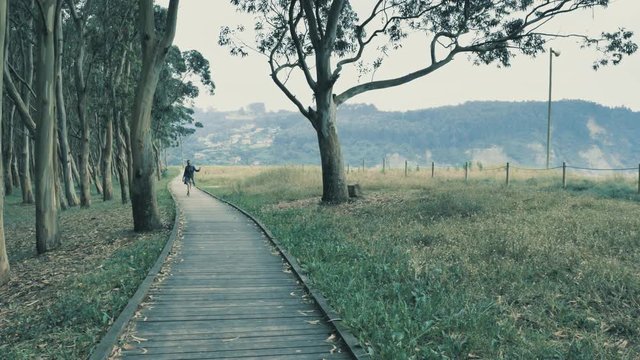 4k pretty young girl walking on the natural wooden podium in the beautiful nature grove with green hills on the background
