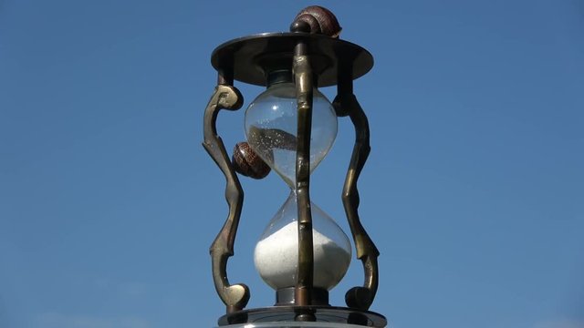 Rotating retro hourglass sandglass with two snail and sand motion on sky background