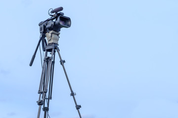 TV camera on tripod on blue sky background.