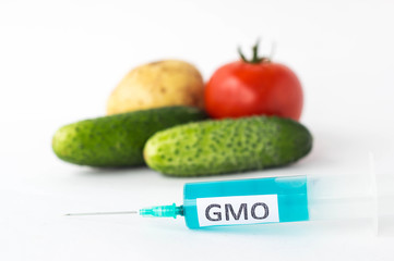 Vegetables on a white background potatoes, cucumbers and tomatoes next to a syringe with an inscription of a gmo, close-up, genetically modified organism