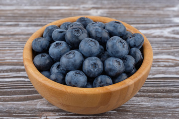 Ripe blueberries in wooden bowl on wood table background. Side view.