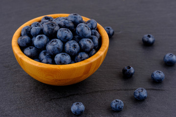 Ripe blueberries in wooden bowl on black stone table background. Side view.