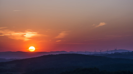 Sunset over the landscape with wind power plants. Sun tightly over the horizon.