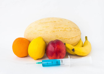 Fruits on a white background bananas, orange, melon, lemon and nectarine, next is a syringe with...
