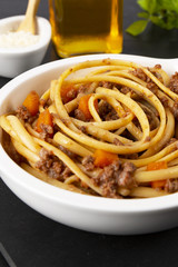 Pasta with bolognese sauce. Parmesan, olive oil, basil. In a white frying pan. The background is black. Italian food.